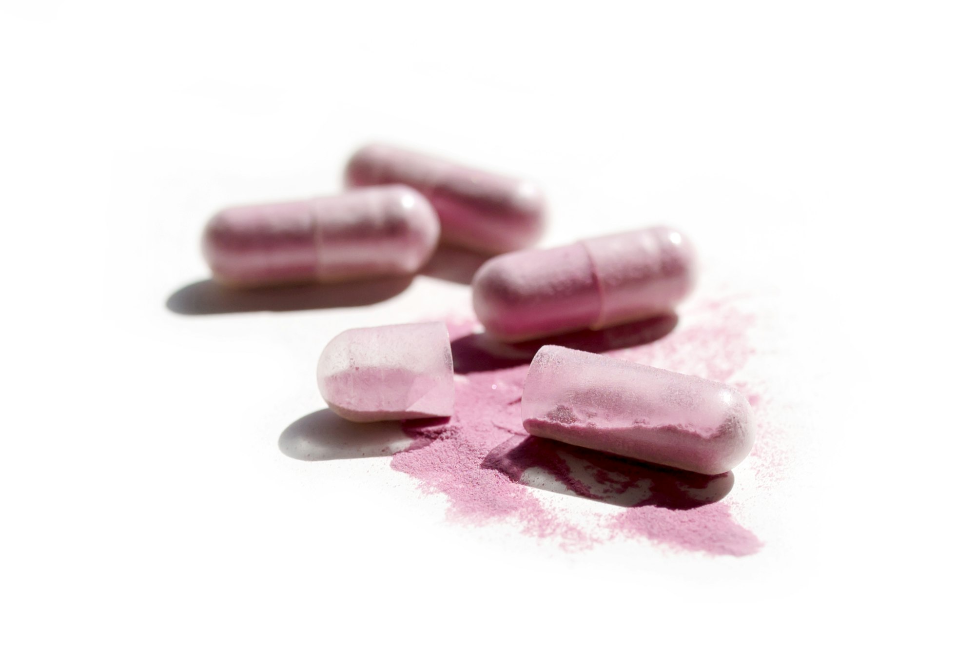 High angle shot of some pink capsules with the internal powder scattered on a white surface