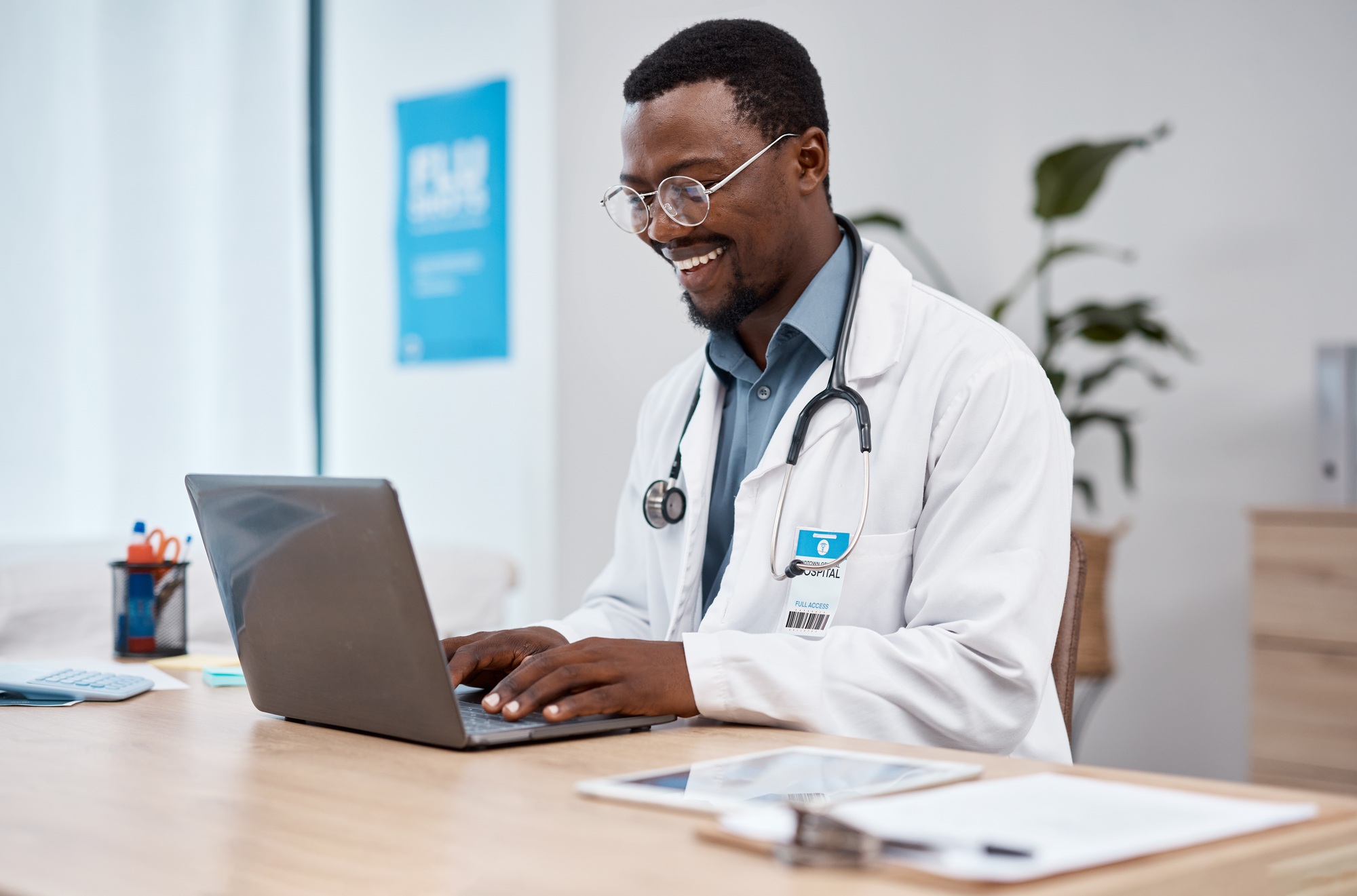 Black man, doctor and laptop with smile in healthcare for research, medicine or PHD at clinic desk.